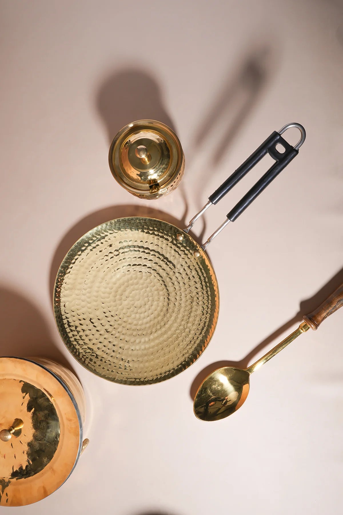 Beautiful brass kitchenware including a strainer, spoon, and container on a neutral background.