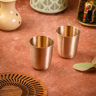 Two elegant golden metal cups on a rustic table with decorative items and a wooden trivet.