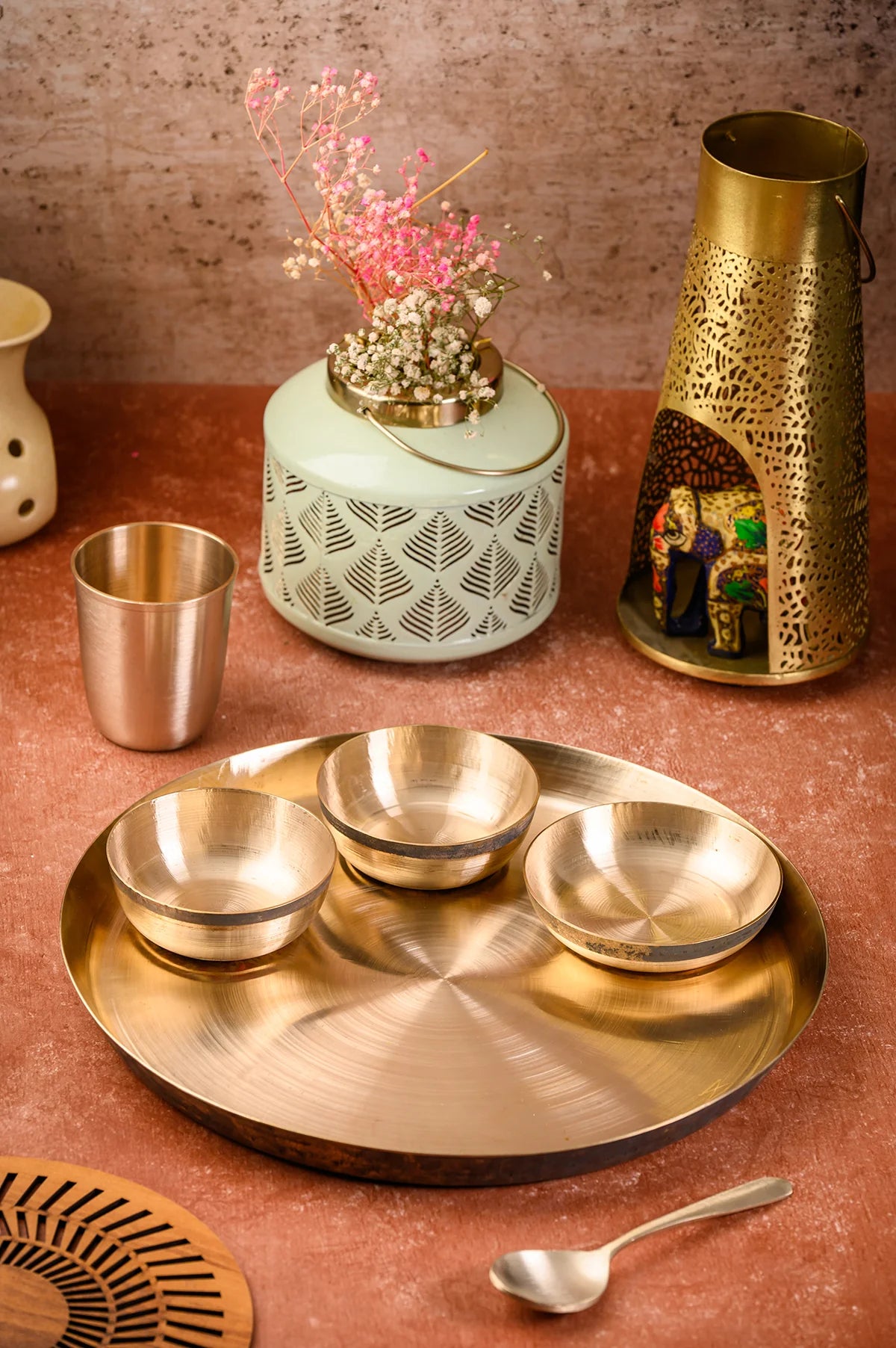 Elegant brass serving platter with bowls, decorative vase, and lantern on a textured background.