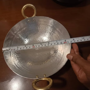 Metallic object with a circular design and measurement scale held by a hand on a wooden surface.