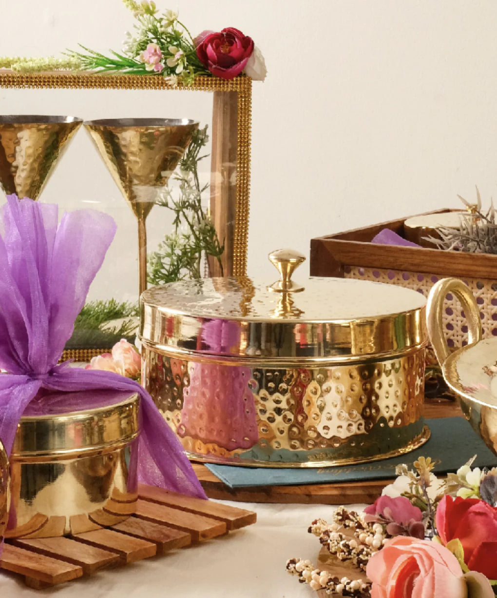 Decorative brass containers with vibrant flowers and elegant glassware on a table.