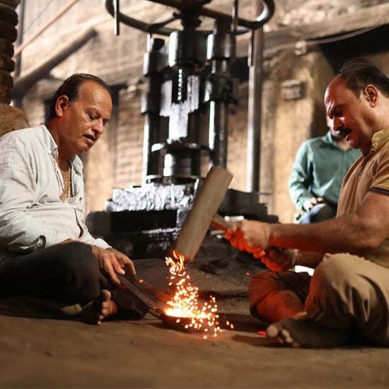 Two craftsmen working with hot metal in a workshop, sparks flying from their tools as they shape the material.