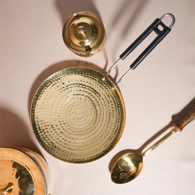 Elegant gold kitchenware featuring a textured serving plate, spoon, and lid against a neutral backdrop.