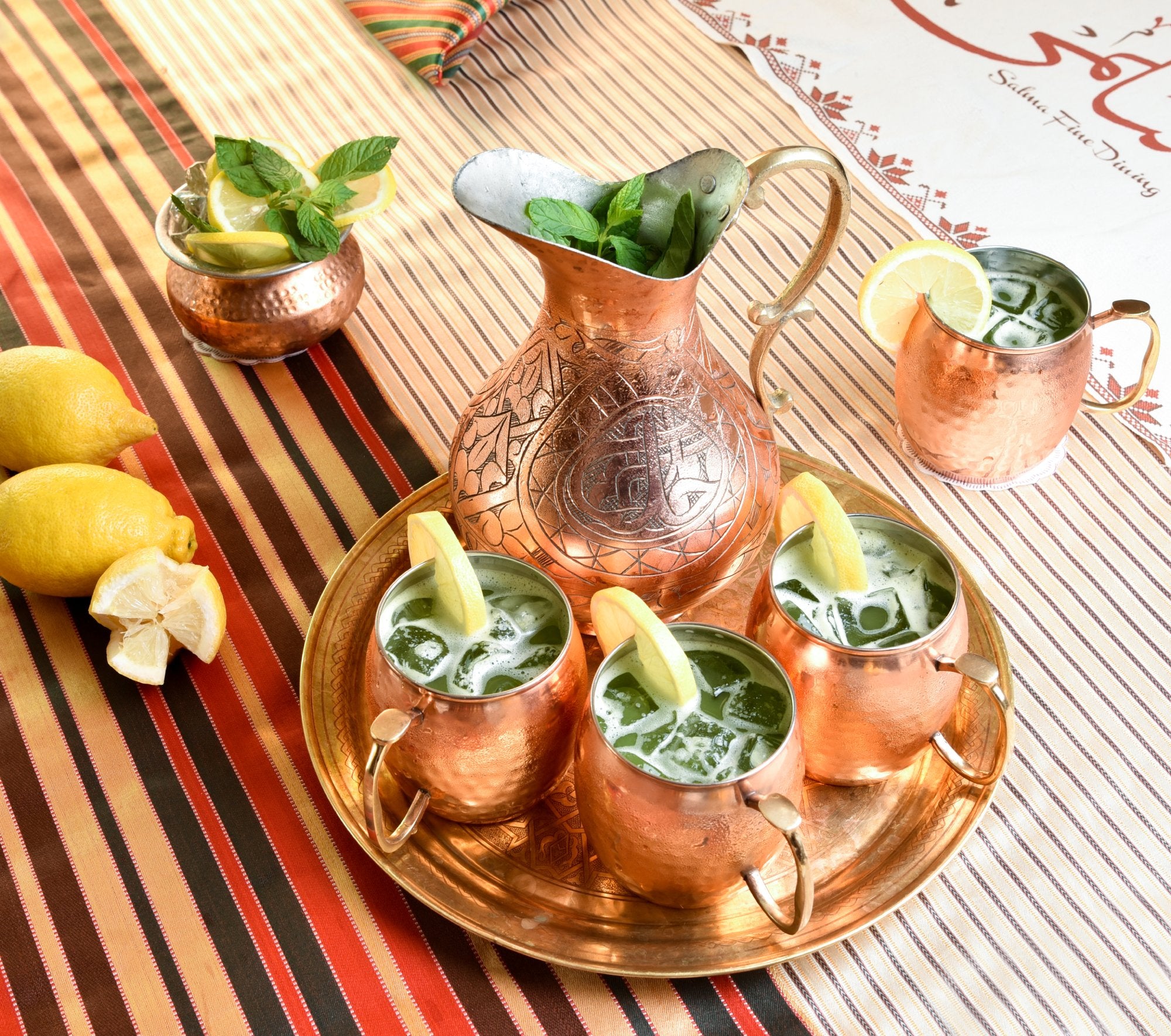 Refreshing mint and lemon drinks in copper mugs, beautifully arranged on a colorful table setting.